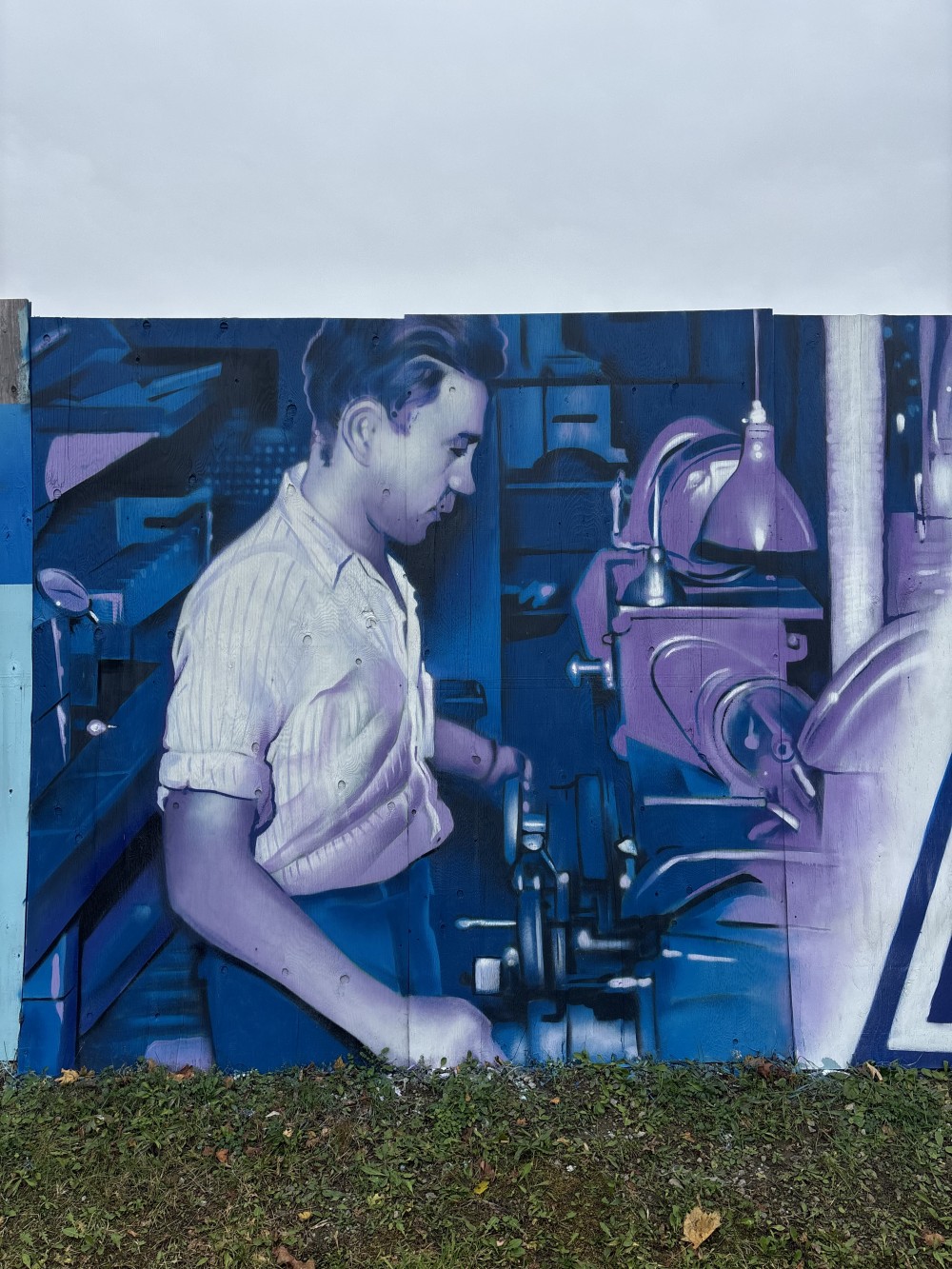 This mural explores industrial heritage and collective labor as the foundation of progress. The work combines archival imagery of workers, engineers, and machinery with the recognizable visual language of a major industrial brand, forming a unified narrative about the era of manufacturing and belief in a technological future.

The composition is structured as a continuous horizontal sequence — an analogy to an assembly line — where human effort, machines, and time operate within a shared rhythm. A cool blue-violet color palette emphasizes the technical nature of the scene while introducing a sense of distance and historical reflection.

The mural engages with the urban environment as an open archive. It does not simply decorate the space, but restores visibility to the people whose everyday, often unnoticed labor shaped the industrial landscape and cultural identity of the twentieth century.