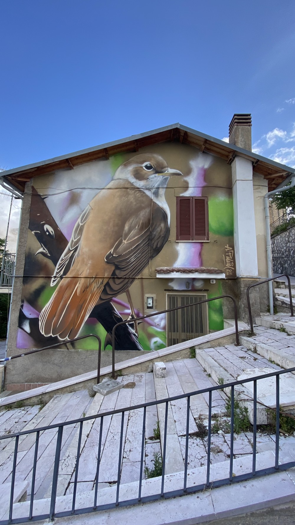 Created in Aielli, Italy, this mural depicts a nightingale—a nocturnal bird known for singing only at night, under the stars. The choice of subject directly connects to Aielli’s identity as a town renowned for its astronomical observatory, where night, sky, and sound become part of everyday life.

The work transforms the building façade into a quiet dialogue between earth and cosmos, nature and observation. The nightingale becomes a symbol of unseen presence, inner voice, and poetic continuity—an homage to the night as a space of reflection, science, and imagination.