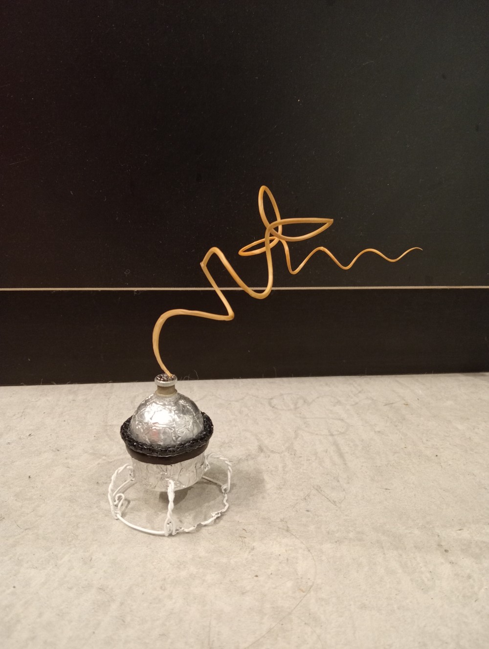 Tealight candle cases, leather, chain, dried squiggly grass; sits in a base made out of a sparkling wine cork wire.