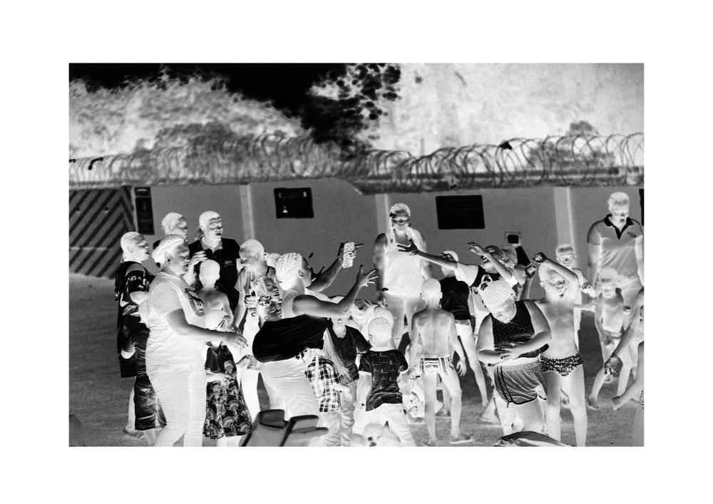 In Reversed Revelry, the art defies convention, flipping light and shadow to cast the familiar into a haunting, dreamlike realm. Figures reach out, frozen in celebration, yet inverted tones turn joyous gestures into something elusive and surreal. Faces and forms, caught in stark monochrome, seem both ghostly and alive, an eerie dance between presence and absence.
There’s a rogue energy here, a rebellion against normality. The crowd distorted yet unified feels like a secret gathering, a moment stolen from reality. The barbed wire in the background reinforces the sense of contained chaos, of liberation within confinement. This art distorts the everyday, demanding viewers confront the duality of human expression: joy shadowed by mystery, connection twisted through a lens of inversion.

Created By Kwaku Kr3