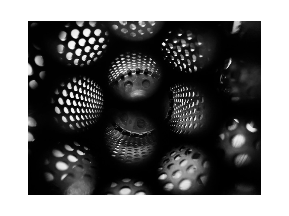 This monochromatic artwork reveals a hypnotic interplay of light and shadow within a perforated structure. The repeating circular patterns evoke a sense of infinite depth, as though peering into a mysterious, otherworldly dimension. The composition draws viewers into its enigmatic core, where light filters delicately through the mesh, creating a symphony of geometric harmony. The abstract quality of the piece allows for diverse interpretations some may see it as a tunnel to the unknown, others as a metaphor for connection and complexity in human life. The stark contrasts of black and white emphasize the balance between presence and absence, clarity and obscurity, suggesting a journey of exploration and introspection. Created By Kwaku Kr3