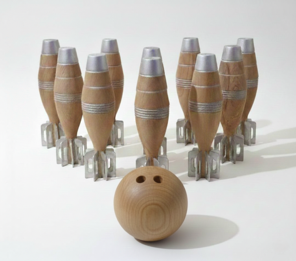The Aesthetics of a Fall argues that modern war technologies produce not only destruction, but also an aesthetic form. The mortar shell, beyond being a product of engineering, persists here as a symbolic sculpture of contemporary violence. The installation questions the place, form, and ideological nature of violence within everyday life.

Wood, as a material, transforms the militaristic form through its fragility and organic quality. Mortar shells shaped like bowling pins make visible the thin line between play and violence. Throughout history, play has functioned as a simulation of war; what appears as an innocent arena is, in fact, a space where violence is intertwined with aesthetics. The installation reveals both the entertaining and traumatic dimensions of play, as each fallen pin signifies the collapse of a body, a structure, or a memory.